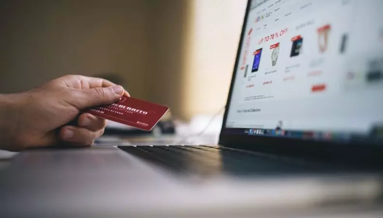 Image of a person holding a payment card in front of a laptop while doing online shopping