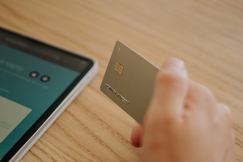 Image of a person holding a payment card next to an electronic device while online shopping